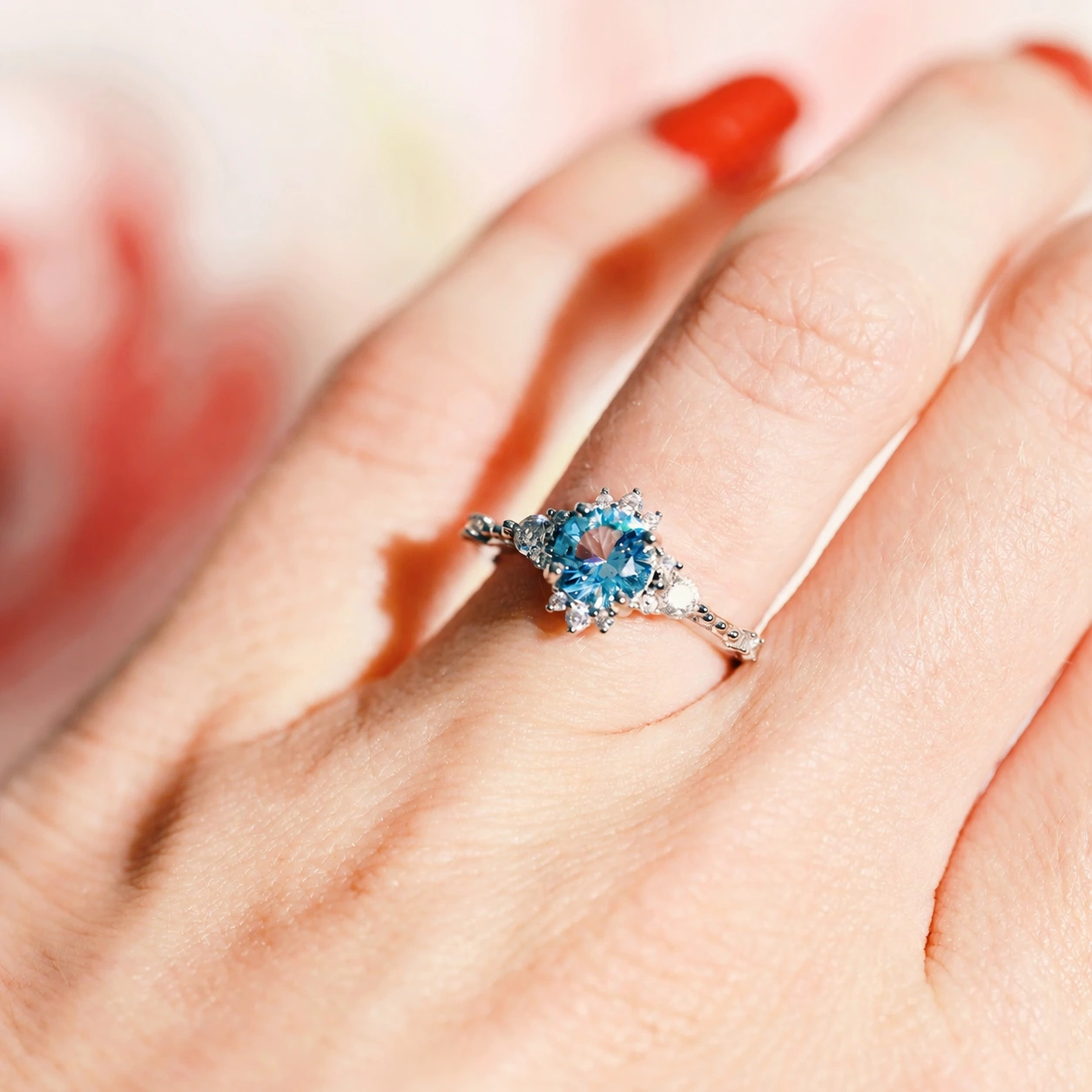Silver ring with blue center and clear accent stones worn on a finger in sunlight